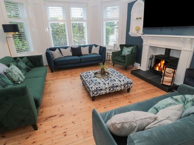 A living room with sofas and an armchair around a patterned ottoman and a fireplace at St Aidans in Alnwick