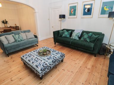 A living room with two sofas a patterned ottoman and framed bird prints on the wall at St Aidans in Alnwick
