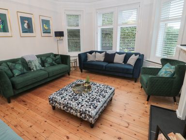 A living room with two green sofas a blue sofa a patterned ottoman and three bird pictures on the wall at St Aidans in Alnwick