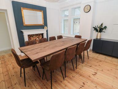 A dining room with a wooden table and chairs a fireplace filled with logs and a cupboard with a vase at St Aidans Alnwick