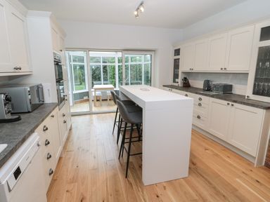 A kitchen with white cabinets an island with chairs and a dining area visible through glass doors at St Aidans in Alnwick