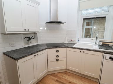 A kitchen with white cabinets black countertop an electric stove a sink next to a window and a wooden floor at St Aidans in Alnwick