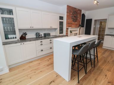 A kitchen with white cabinets a gray countertop a white island with black stools and a brick wall with a clock at St Aidans in Alnwick