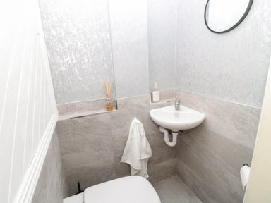 A small bathroom with a toilet a corner sink a round mirror and a hand towel at St Aidans in Alnwick