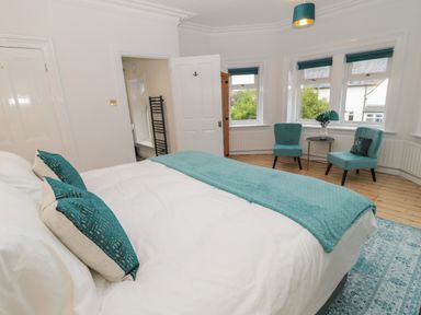 A bedroom with a bed with teal pillows and a teal throw two teal chairs with a small round table near windows at St Aidans in Alnwick