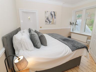 A bedroom with a bed and pillows next to windows with blinds and a bedside lamp at St Aidans in Alnwick