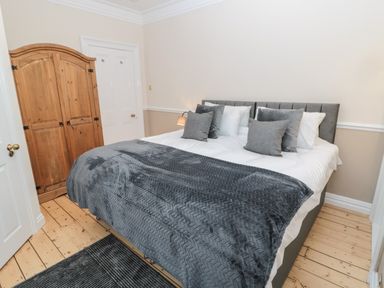 A bedroom with a large bed covered with white sheets and grey pillows and blanket and a wooden wardrobe in the corner at St Aidans in Alnwick