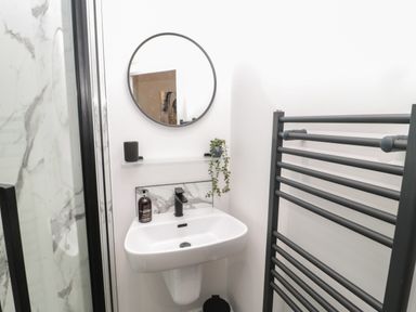 A bathroom sink with a round mirror above and a black towel rack to the right at St Aidans in Alnwick