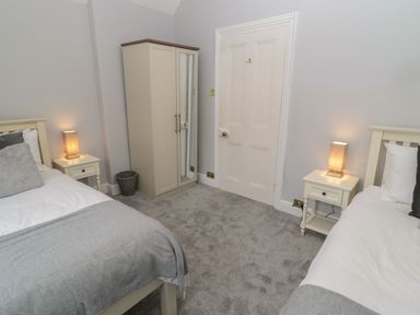 A bedroom with two single beds each with a bedside table and lamp a wardrobe and a door at St Aidans in Alnwick