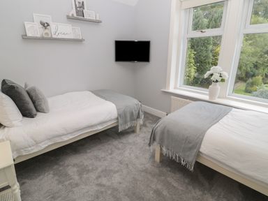 A bedroom with two single beds grey carpet and a wall mounted tv at St Aidans in Alnwick