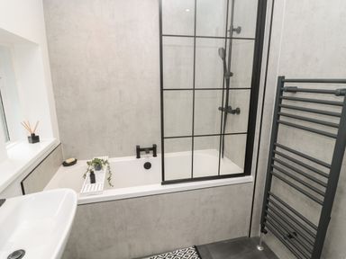 A bathroom with a bathtub shower with black fixtures a white sink and a black heated towel rail at St Aidans in Alnwick