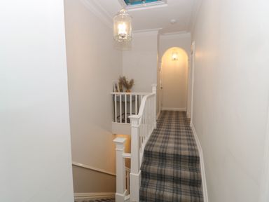 A hallway with plaid carpet covering stairs and floor with white walls and railing at St Aidans in Alnwick