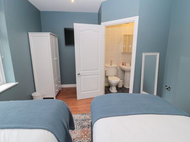 A bedroom with two beds blue blankets a white wardrobe an open door to a bathroom and a wall-mounted television at St Aidans in Alnwick