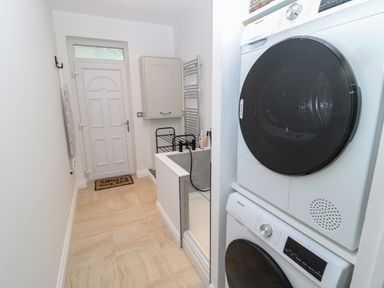 A laundry room with stacked washer and dryer a door a cabinet and a small utility sink at St Aidans in Alnwick