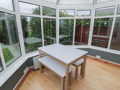 A small white table with a bench and stool in a conservatory with wooden floors and large windows at St Aidans in Alnwick