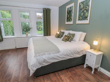 A bedroom with a bed white bedding green pillows green curtains wooden floor and nightstand with lamp at St Aidans in Alnwick