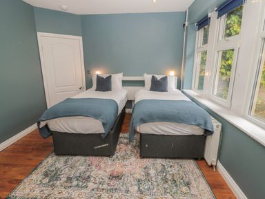 A bedroom with two single beds side by side a patterned rug wooden floor and windows on one side at St Aidans in Alnwick