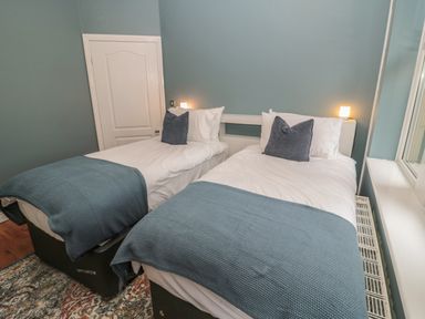 A bedroom with two single beds made with white sheets and blue throws at St Aidans in Alnwick