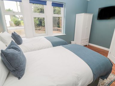 A bedroom with two single beds and blue bedding a white wardrobe and a wall-mounted TV at St Aidans in Alnwick
