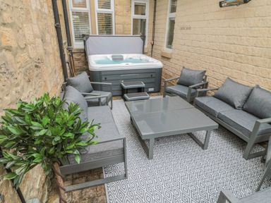 An outdoor seating area with a gray sofa set around a square table and a hot tub in a stone-walled courtyard at St Aidans in Alnwick