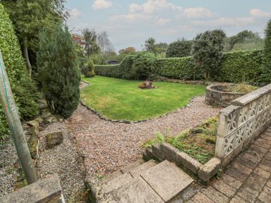 A garden with a lawn gravel paths trees and shrubs with a low concrete wall at St Aidans in Alnwick