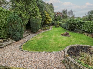 A garden with a gravel path around a lawn surrounded by bushes and trees at St Aidans in Alnwick