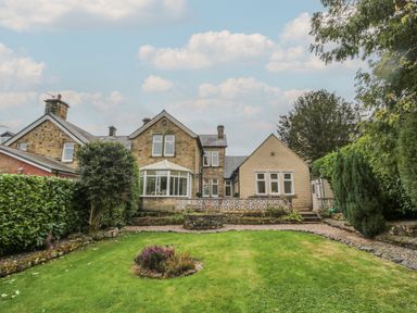 The back view of a stone and brick house with a conservatory and garden with lawn and shrubs at St Aidans in Alnwick