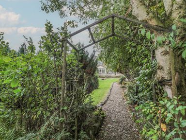 A garden pathway with gravel and greenery forming an archway leading to a house at St Aidans in Alnwick