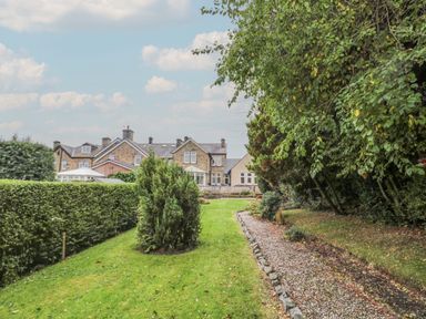 A grassy garden area with trimmed hedges and trees near a stone house at St Aidans in Alnwick