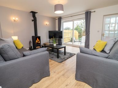 A living room with two gray sofas and yellow cushions a black coffee table a wood stove and a television near sliding glass doors at Harran Annex in Peopleton