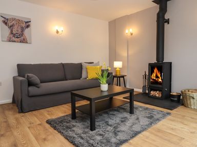 A living room with a gray sofa yellow cushions a black coffee table with flowers a wood burning stove and a lamp at Harran Annex in Peopleton