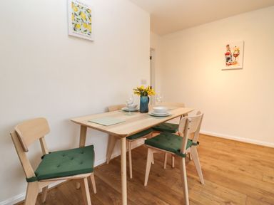 A dining area with a wooden table and four chairs with green cushions a vase with yellow flowers and tableware on a wooden floor at Harran Annex in Peopleton