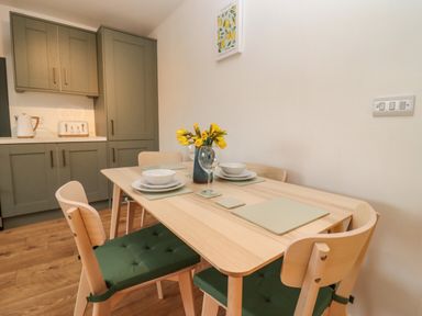 A dining area with a wooden table set with bowls plates placemats and glasses four chairs with green cushions and kitchen cabinets in the background at Harran Annex in Peopleton