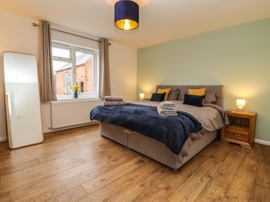 A bedroom with a double bed, bedside tables with lamps, a full-length mirror, and a window with curtains at Harran Annex in Peopleton