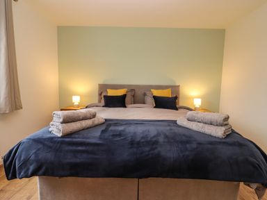 A bedroom with a double bed with folded towels on it two bedside tables with lamps at Harran Annex in Peopleton