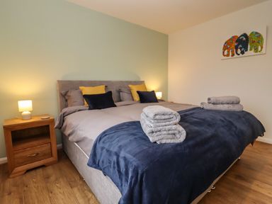 A bedroom with a double bed with pillows and folded towels on top and wooden nightstands with lamps at Harran Annex in Peopleton