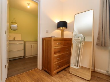A room with a wooden chest of drawers with a lamp on top and a standing mirror reflecting a white shelving unit at Harran Annex in Peopleton