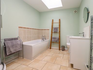 A bathroom with a bathtub a towel rack a wooden ladder with towels a toilet a sink and a mirror at Harran Annex in Peopleton