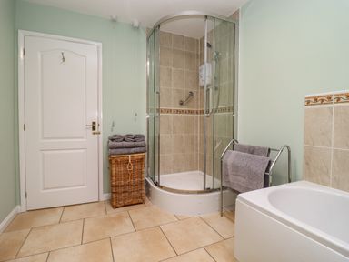 A bathroom with a glass shower enclosure a white bathtub a wicker laundry basket with towels and a towel rack at Harran Annex in Peopleton