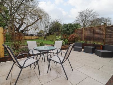 An outdoor patio with a glass round table and four chairs near a garden at Harran Annex in Peopleton