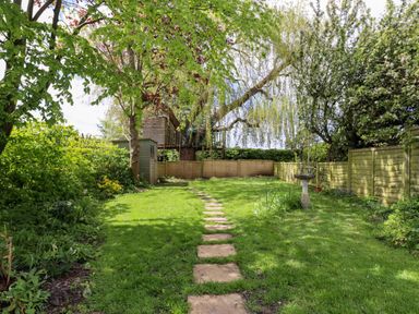 A garden with a stone path leading to a treehouse and a birdbath surrounded by trees and fences at Harran Annex in Peopleton