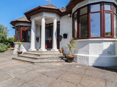 An entrance with white pillars and steps leading to a door with potted plants on a patio at Penang in St Austell