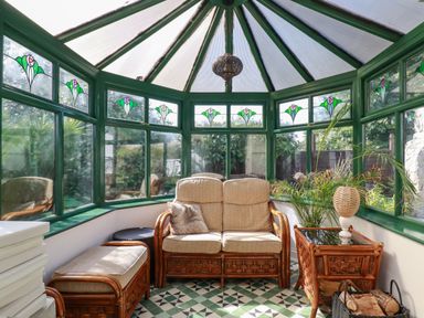 A conservatory with stained glass windows rattan furniture and a tiled floor at Penang in St Austell