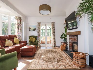 A living room with green and brown chairs a patterned rug a fireplace and a wall-mounted TV at Penang in St Austell