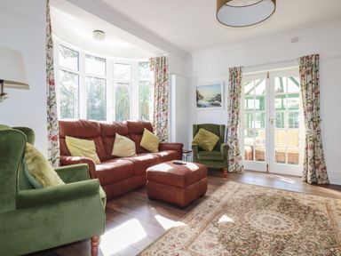 A living room with green armchairs a brown sofa and ottoman with floral curtains and a rug at Penang in St Austell