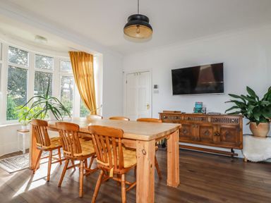 A dining room with a wooden table and chairs a television on the wall and plants at Penang in St Austell