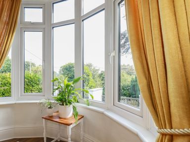 A corner with large windows and a small table with two potted plants and yellow curtains at Penang in St Austell