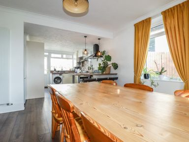A dining area with a wooden table and chairs next to a kitchen with pendant lights and plants at Penang in St Austell