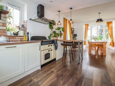 A kitchen with a stove and counter leading to a dining area with a wooden table and chairs with large windows at Penang in St Austell