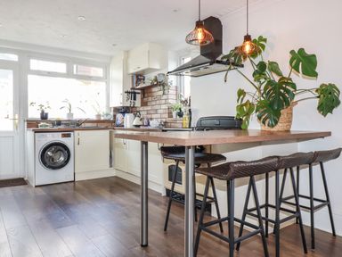 A kitchen with a washing machine countertop stools and plants on the table at Penang in St Austell